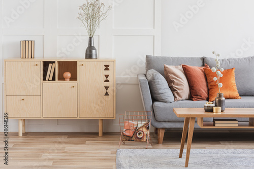 木制家具和灰色的斯堪的纳维亚沙发与枕头在美丽的客厅内部