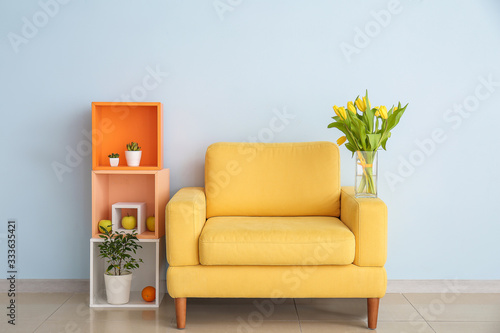 现代房间的内部有舒适的扶手椅，架子单元和春天的花朵靠近轻墙