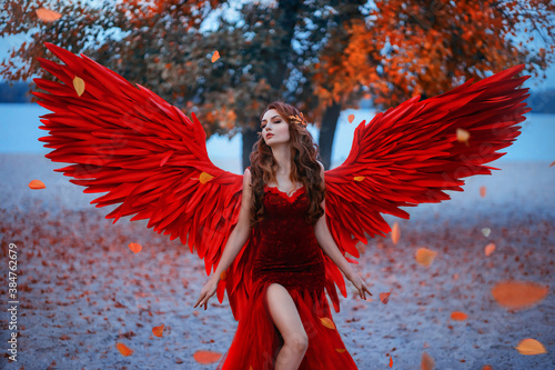 年轻美丽的女人堕落天使站在公园附近的树与橙色的落叶。Creati